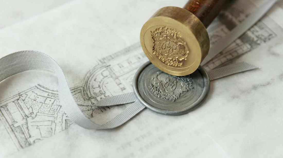 What Is Sealing Wax? A close-up view of a metal seal stamp pressing into silver wax over a delicate architectural drawing.